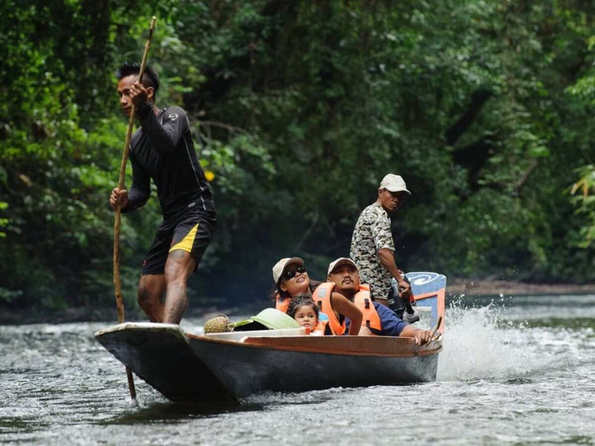 Traditional wooden longboat on Batang Ai Lake heading towards a riverside Iban longhouse in the rainforest