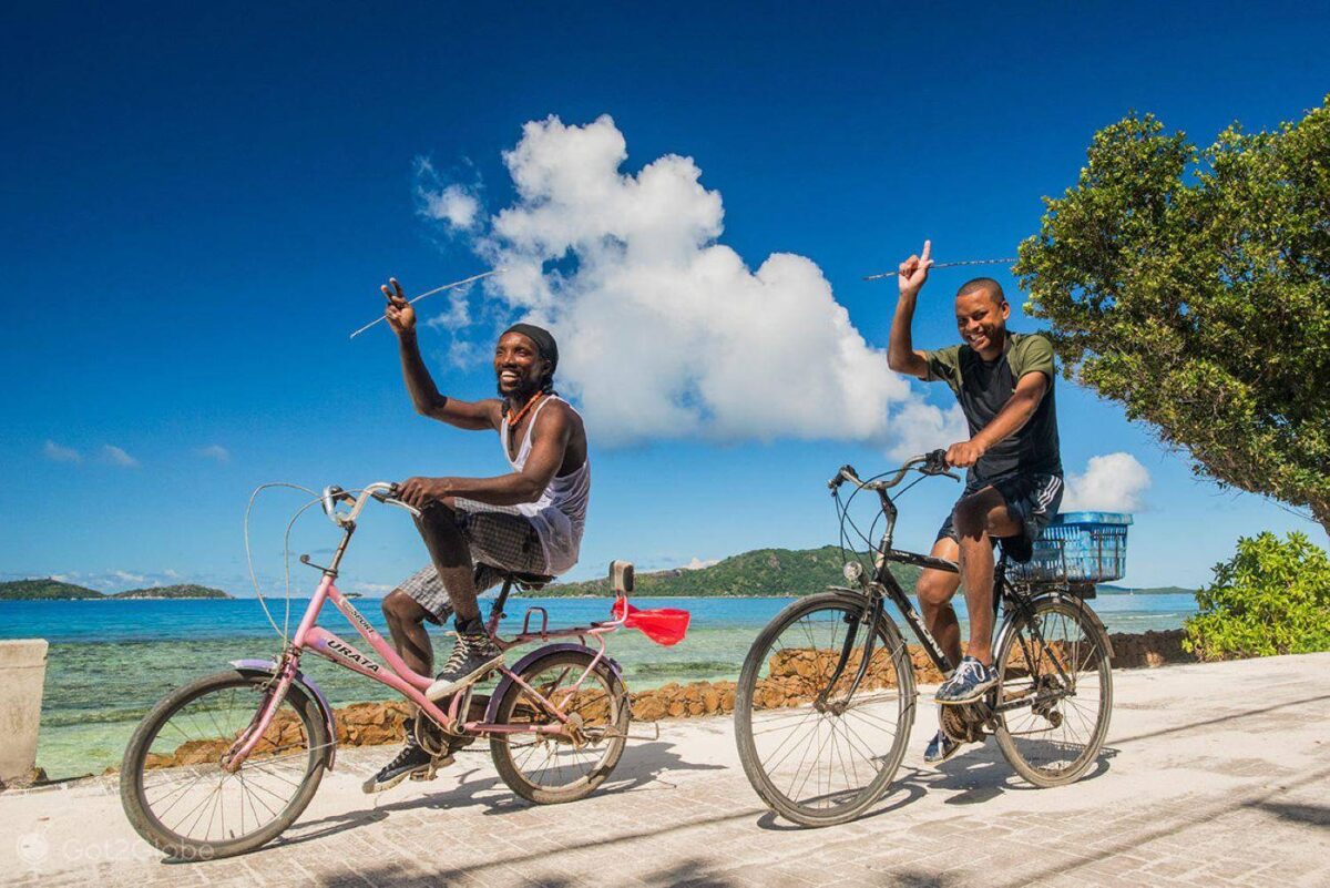 Traveler cycling along a palm-lined road towards the beach on La Digue