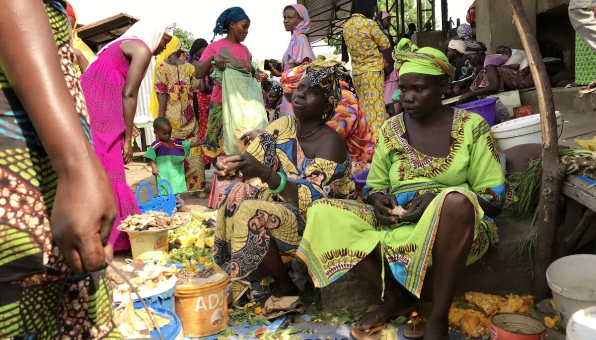 Travellers sitting on mats sharing a communal Senegalese meal with villagers in a shaded courtyard