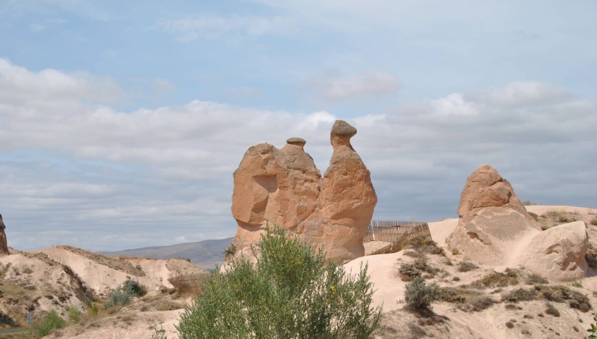 Trekker crossing Cappadocia’s Güllüdere Valley with pink-tinted cliffs and rock-cut dwellings near Cavusin