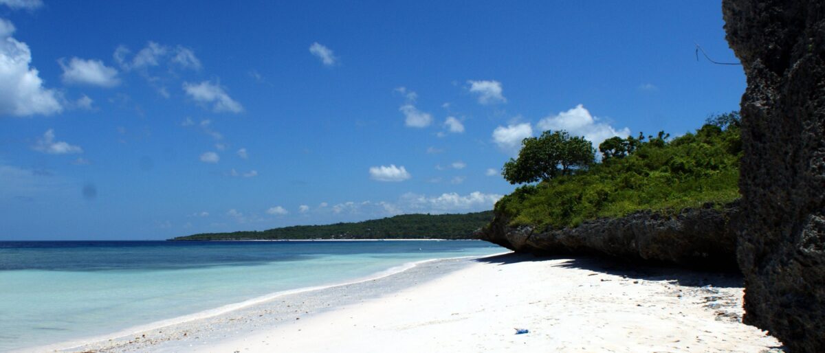 Tropical beach at Bira with white sand, palm trees, calm turquoise sea and a diver preparing to enter the water