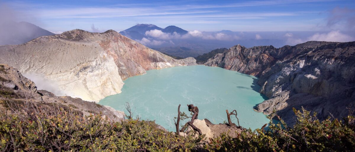 Turquoise crater lake of Mount Ijen with rising sulfur fumes at sunrise