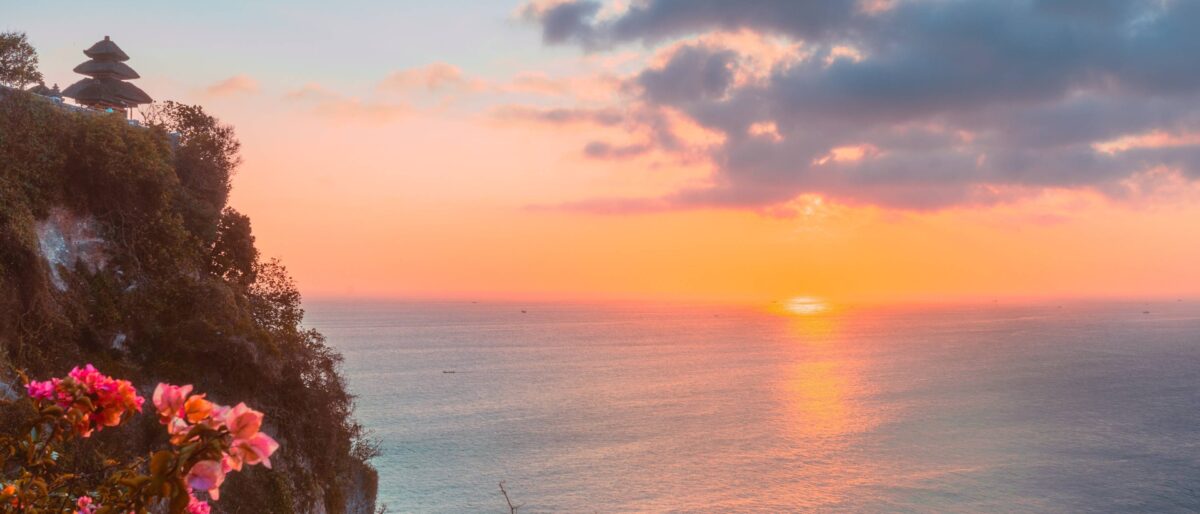 Uluwatu Temple perched on a high cliff above the ocean at sunset with waves crashing below