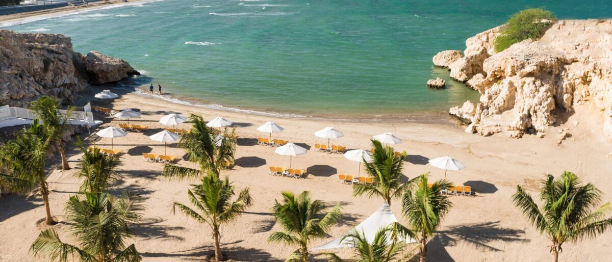 View of Muscat coastline with white buildings, mountains and the sea under a clear sky