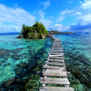 View over turquoise sea, white-sand beach and lush green islands in Raja Ampat, Indonesia, under a bright tropical sky