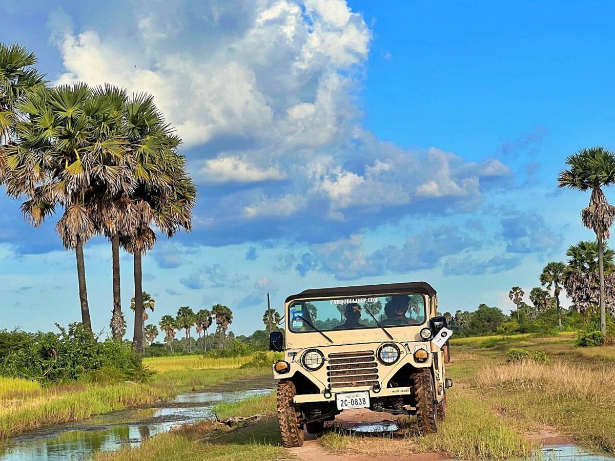 Vintage open-top jeep parked near the intricately carved pink sandstone temple of Banteay Srei in Cambodia