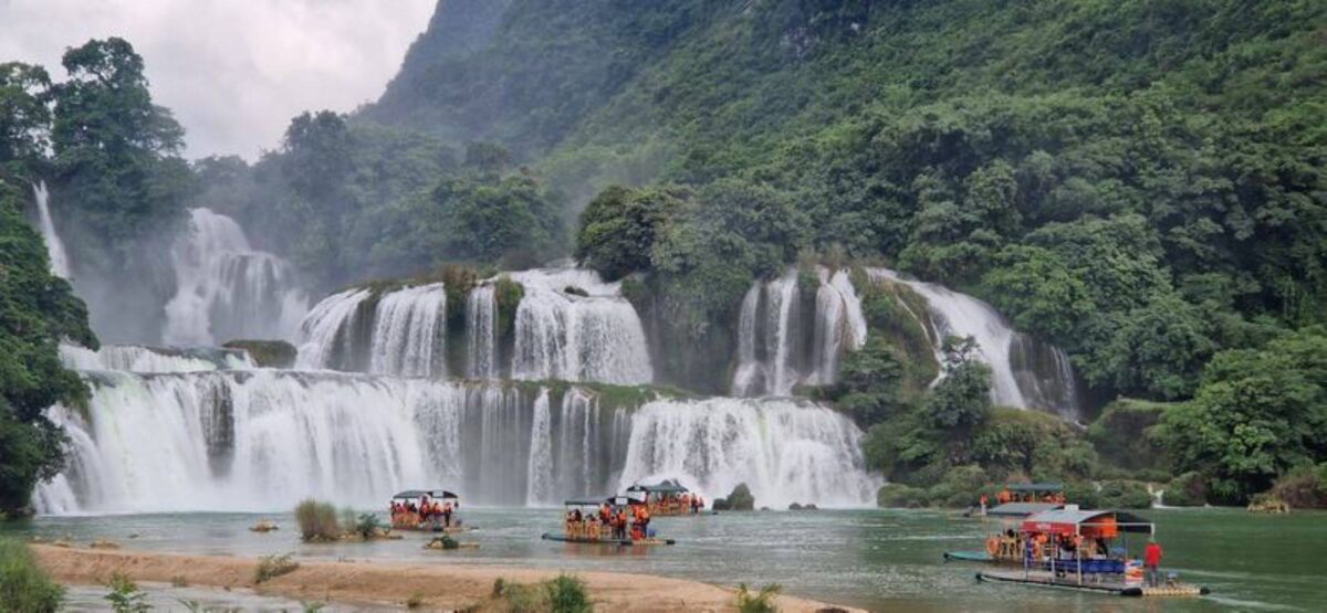 Wide view of the tiered Ban Gioc waterfalls cascading over green limestone terraces into a turquoise pool on the Vietnam–China border