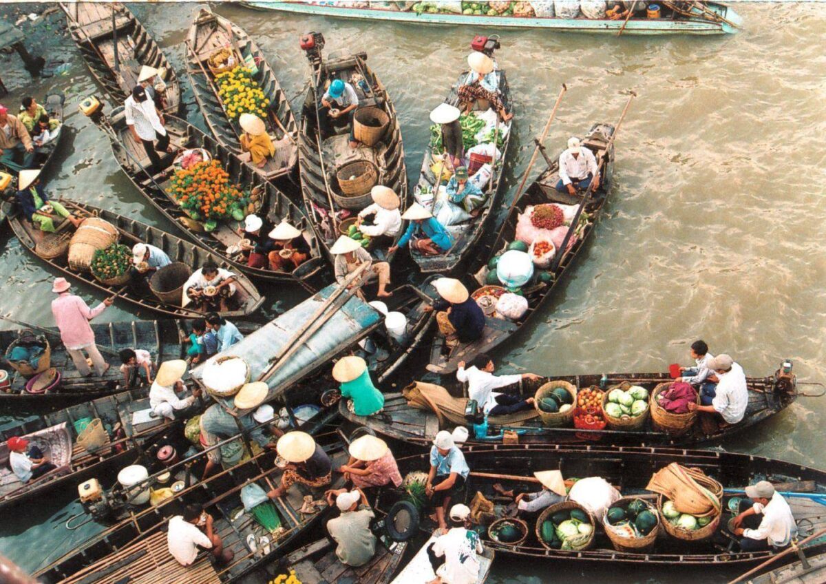 Wooden boat cruising along a narrow canal lined with lush tropical vegetation in the Mekong Delta near Cai Be, Vietnam