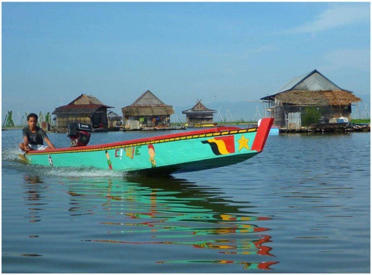 Wooden floating houses on Lake Tempe at sunset with a small motorized canoe and reflections on calm water